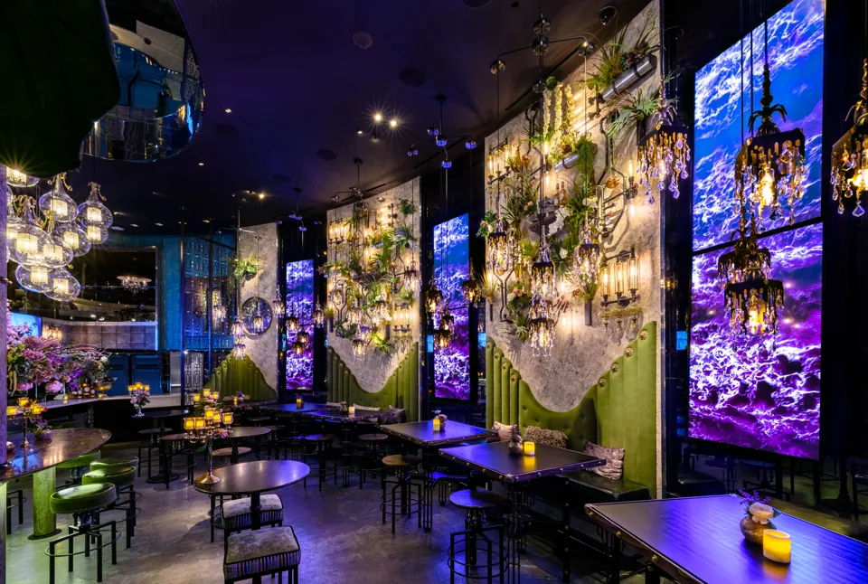 Mesas, asientos verdes y lámparas del interior de Vanderpump Cocktail Garden en Caesars Palace
