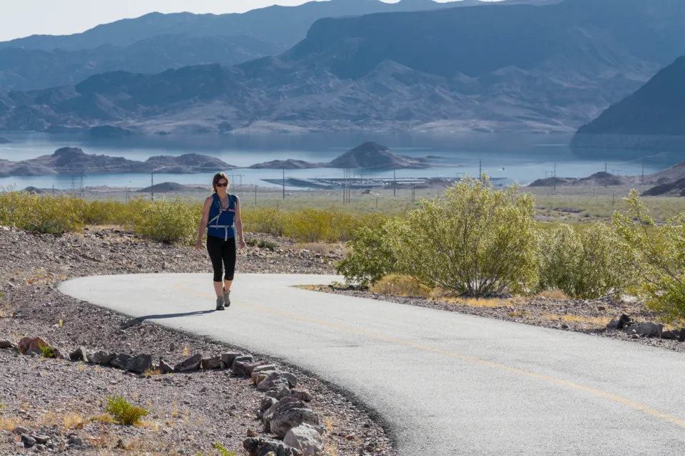 Una caminante en el sendero pavimentado River Mountains Loop Trail con Lake Mead al fondo.