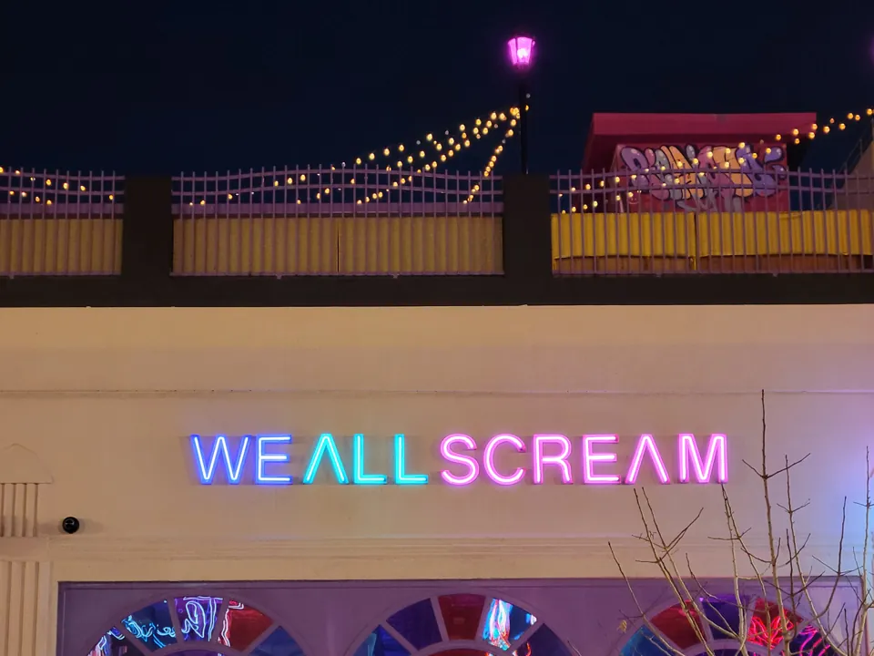 Letrero luminoso We All Scream y parte de su azotea al anochecer.