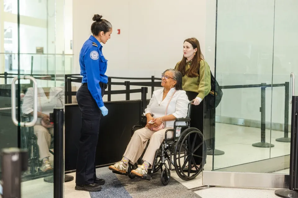 Agente de TSA conversa con una pasajera en silla de ruedas y su acompañante en BWI; archivo de abril de 2025.